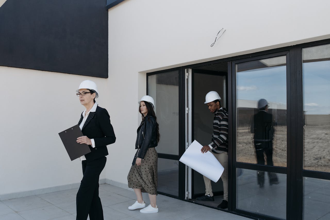 Real estate agents wearing hard hats evaluate plans outside a modern building.